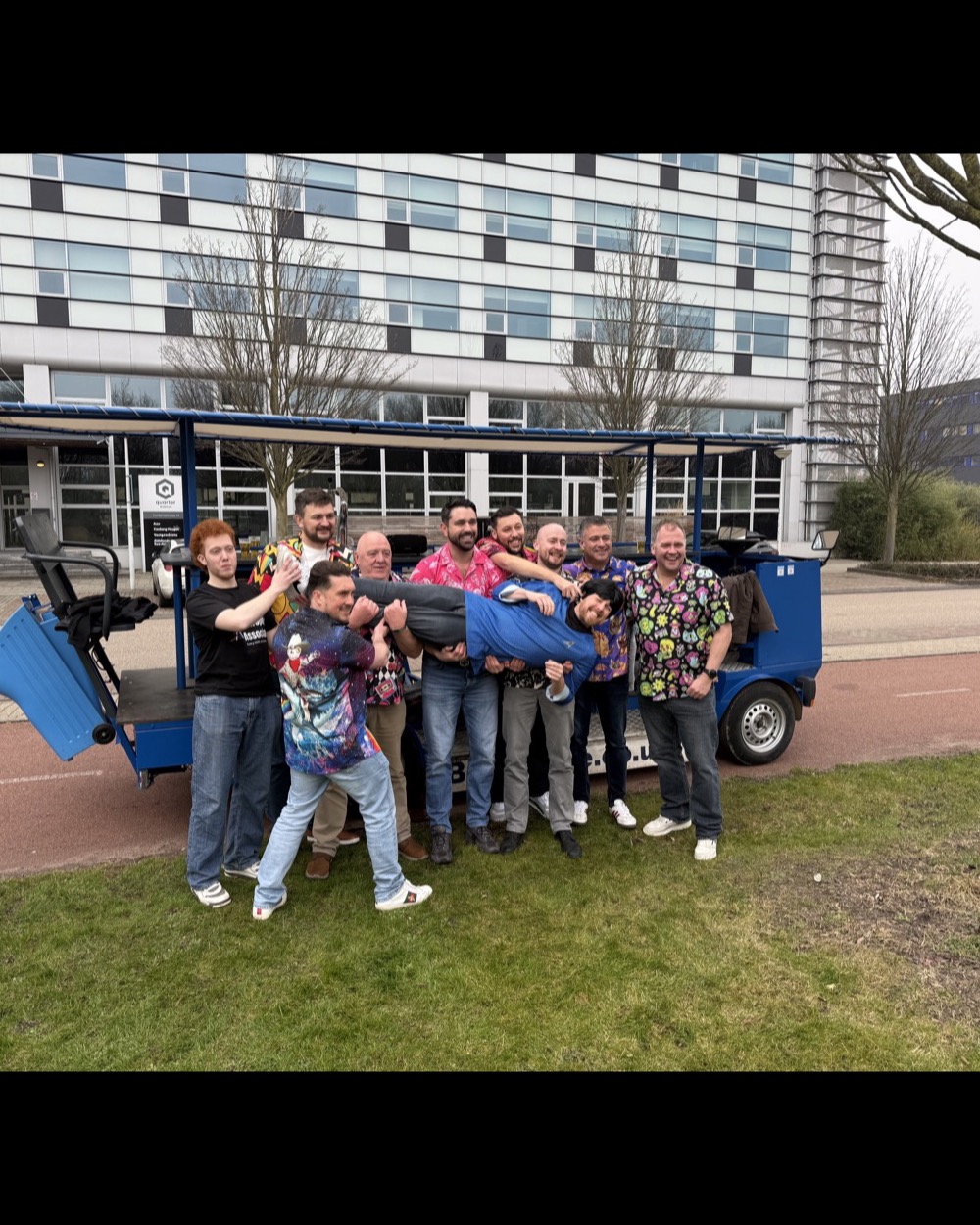 Stag-party group lifting a friend in front of a DamTours beer bike